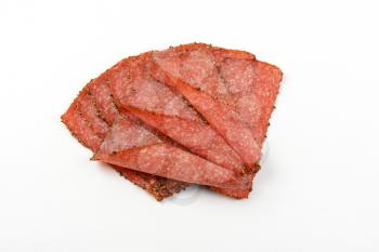 Thin slices of pepper coated salami on white background