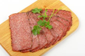 Thin slices of pepper coated salami on wooden cutting board