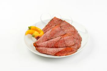 Thin slices of pepper coated salami on white plate
