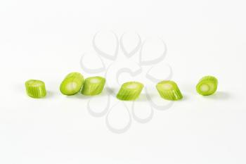 slices of green onion in a row on white background