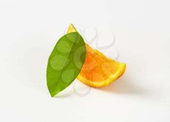 Single orange wedge with leaf on white background