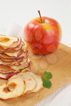 stack of dried apple chips and fresh apple on wooden cutting board - close up
