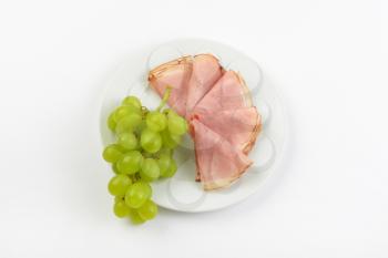 plate of ham slices with bunch of white grapes