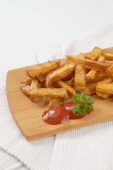 heap of fried chipped potatoes with ketchup on wooden cutting board