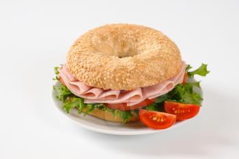 sesame bagel sandwich with ham on white plate