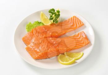 raw salmon fillets with lemon and parsley on white plate