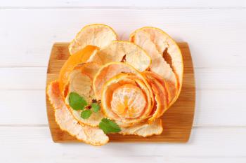 peeled tangerine arranged in peels on wooden cutting board