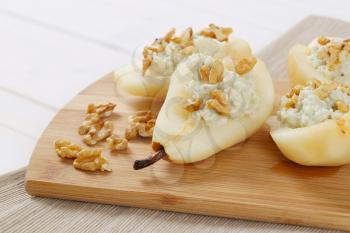 halved pears with blue cheese and walnuts on wooden cutting board - close up