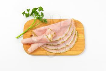 slices of asparagus coated ham with parsley on wooden cutting board