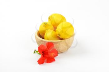 bowl of ripe lemons and red hibiscus bloom on white background