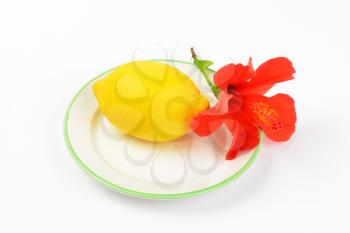 ripe lemon with red hibiscus bloom on white plate