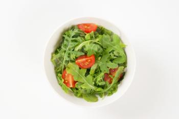 bowl of arugula and tomato salad on white background