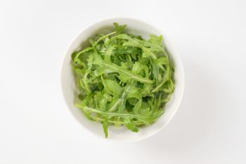 bowl of fresh arugula leaves on white background