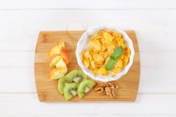 bowl of corn flakes with milk and fresh fruit on wooden cutting board
