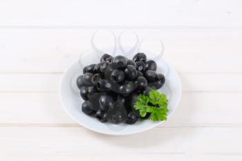 plate of black olives with fresh parsley on white background