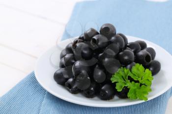 plate of black olives with fresh parsley on blue place mat - close up
