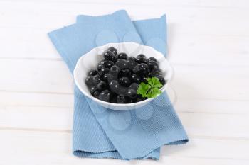 bowl of black olives with fresh parsley on blue place mat