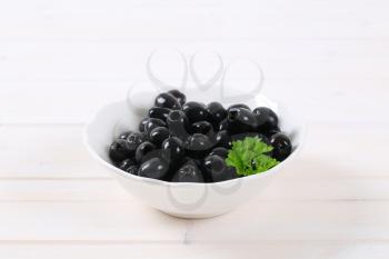 bowl of black olives with fresh parsley on white background