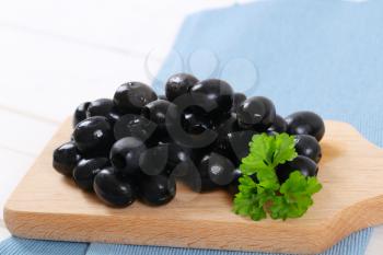 pile of black olives with fresh parsley on wooden cutting board - close up