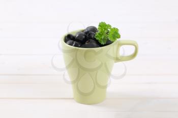 cup of black olives with fresh parsley on white background