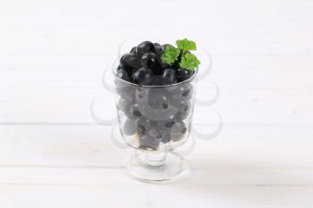 glass of black olives with fresh parsley on white background