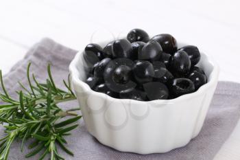 bowl of black olives with fresh rosemary on grey place mat - close up
