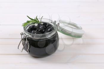 jar of black olives with fresh rosemary on white background