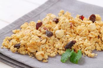 pile of morning granola with hazelnuts, raisins and cranberries on grey place mat - close up