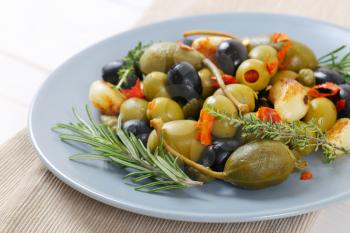 Plate of green and black olives with garlic, capers and caper berries