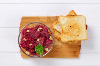 bowl of fresh beetroot spread with toast on wooden cutting board