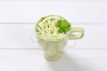 cup of raw zucchini noodles on white wooden background