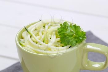 cup of raw zucchini noodles on grey place mat - close up