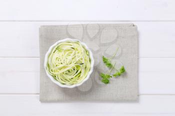 bowl of raw zucchini noodles on beige place mat
