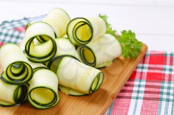 raw zucchini strips rolled on wooden cutting board - close up