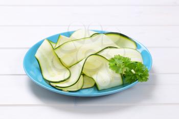 plate of raw zucchini strips on white wooden background