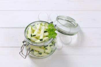 jar of zucchini strips on white wooden background