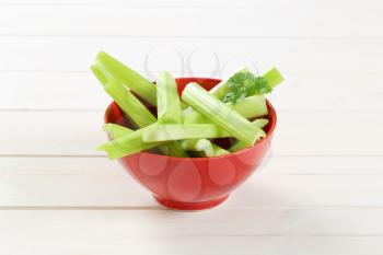 bowl of green celery stems on white wooden background