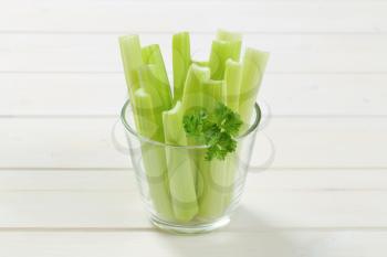 glass of green celery stems on white wooden background