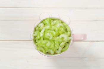 cup of chopped celery stems on white wooden background