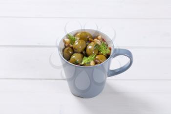 cup of marinated green olives on white wooden background