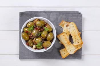 bowl of marinated green olives with toast on grey place mat