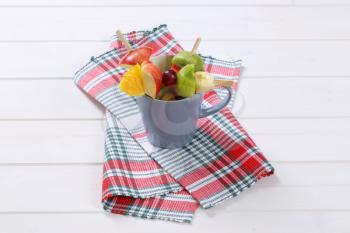 cup of fresh fruit skewers on checkered dishtowel