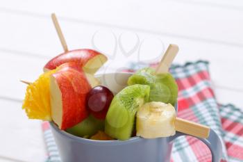 cup of fresh fruit skewers on checkered dishtowel - close up