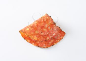 Thin slice of black pepper-coated salami speckled with pieces of Comte cheese