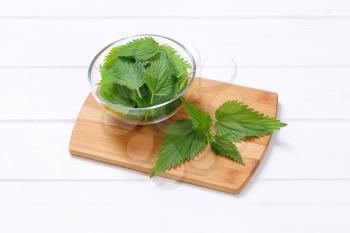 bowl of fresh nettle leaves on wooden cutting board