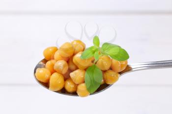 spoon of cooked chickpeas on white wooden background