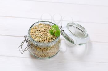 jar of dry brown lentils on white wooden background