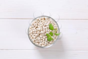 glass of raw white beans on white wooden background