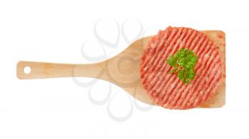 raw hamburger patty on wooden spatula