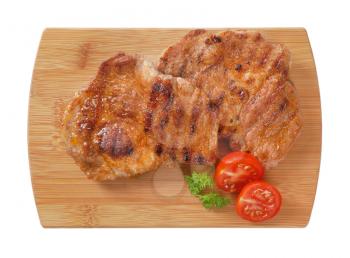 two slices of grilled pork meat on wooden cutting board